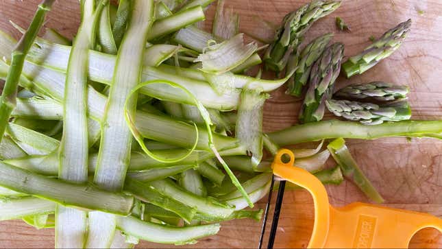 Asparagus shavings and tips on a wooden cutting board with a vegetable peeler.